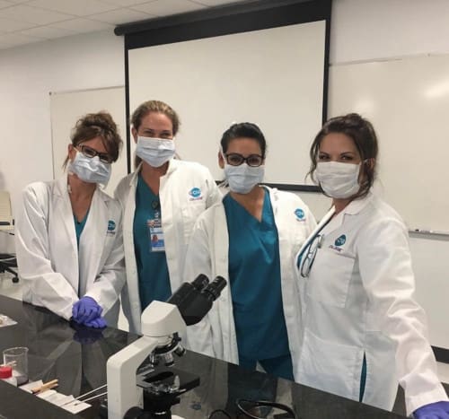 A group of nursing students standing at a table with a microscope