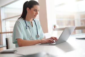 A LVN sitting at a desk using a laptop.