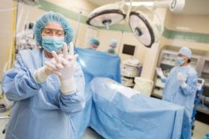 A surgical technologist in an operating room putting on latex gloves.