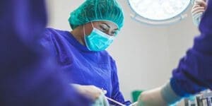 A surgical assistant wearing a mask working with a surgeon in an operating room.