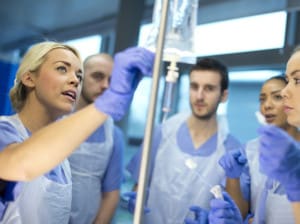 Four BSN students with aprons and gloves learning to use an IV bag.