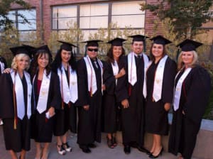 A group of 8 CNI graduates wearing caps and gowns standing outside of the school.