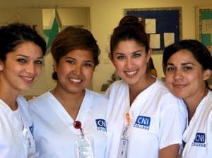 Four CNI students wearing scrubs smiling at the camera.