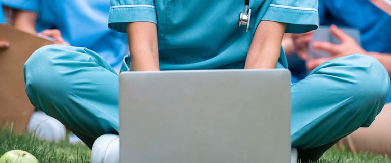 Nurse sitting in grass with a laptop opened in front of her.