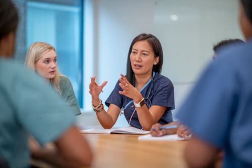 A nurse explains information to other nurses who are sitting at a table