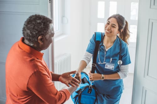 A nurse being greeted at the door of a house by an elderly man.