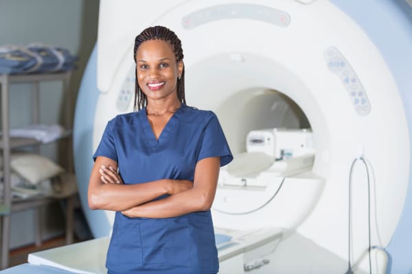 AN MRI Technician in scrubs standing in front of an MRI machine.