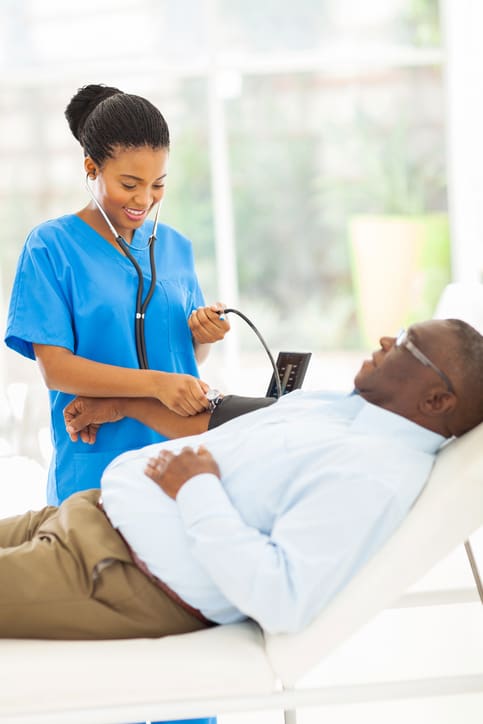 A nurse taking the blood pressure of a patient that is laying on a bed