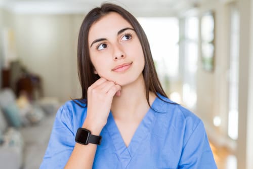 Nurse in scrubs with her fist under her chin looking up and thinking.