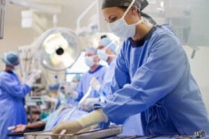 A surgical technician working in an operating room with a surgery in the background.