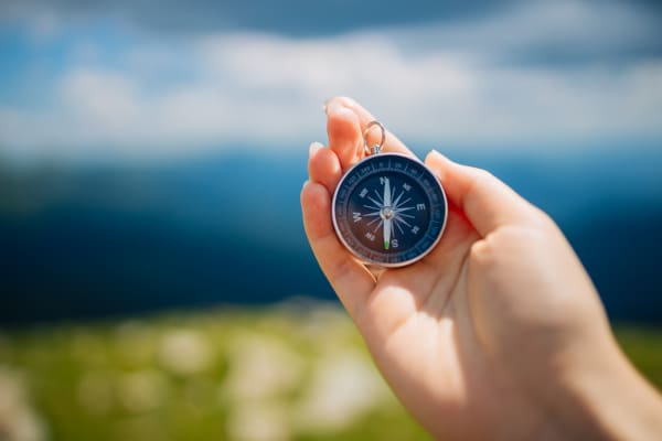 Hand holding a compass with a lake in the background