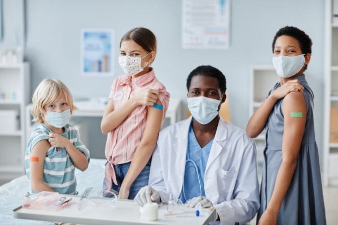 A nurse sitting with 3 children after they've gotten vaccinations