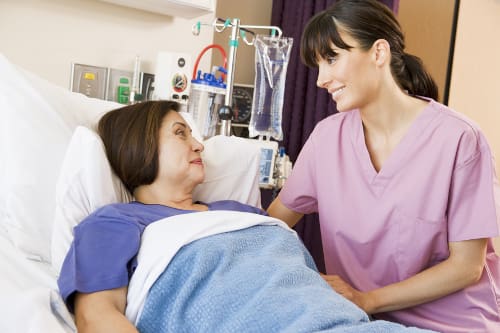 A nurse talking to a patient that is laying on a hospital bed