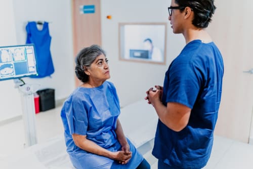 A male nurse talking to a female patient that is sitting in a doctor's office