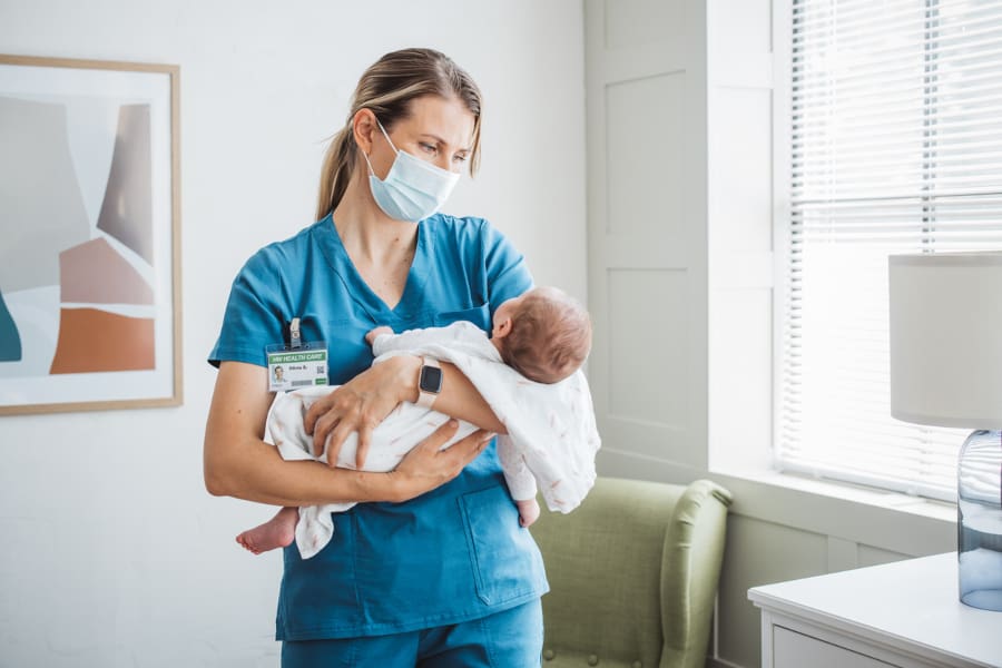 A pediatric nurse holding a baby in a patient room