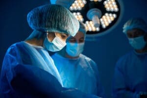 A surgeon working on a patient in an operating room with two assistants behind her